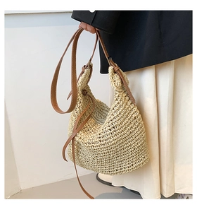 Close-up of woven straw tote bag with brown leather strap and side drawstring detail