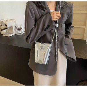 Detail of silver metallic bucket bag with chain strap and rotary lock on model