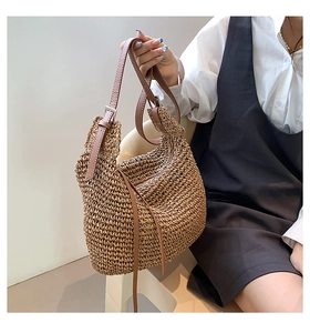 Close-up of woven straw tote bag featuring brown leather strap and metal buckle detail