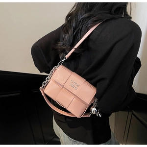 Détail du sac bandoulière rose tressé avec chaîne argentée et logo métallique gravé