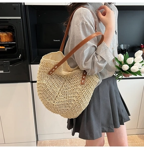 Close-up of woven straw tote bag featuring brown faux leather straps and contrast stitching