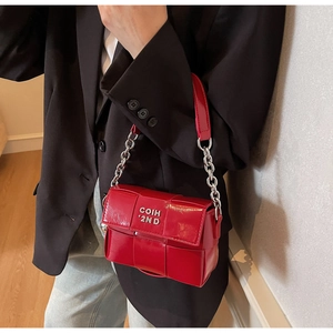 Gros plan d'un sac à main tissé rouge vif avec chaîne argentée sur une veste noire