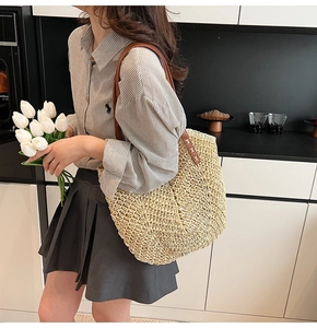 Detail of hand-woven straw tote bag with brown leather shoulder strap and rivet accents