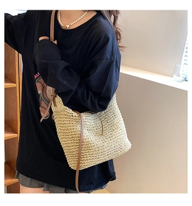 Detail of hand-woven beige straw tote bag with brown leather knotted shoulder strap
