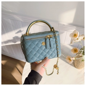 Close-up of light blue quilted crossbody bag with gold camellia clasp and chain handle