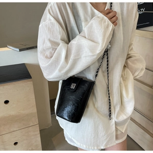 Detailed view of a black glossy leather bucket bag with a stylish metal chain strap