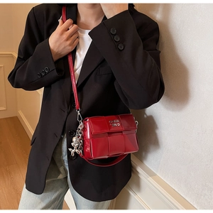 Détail du sac bandoulière rouge tissé avec logo argenté et breloque ours mignon