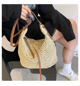 Detailed close-up of natural beige straw tote bag with woven texture and brown leather straps