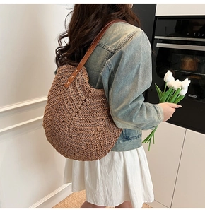 Detail of hand-woven straw tote bag with brown leather shoulder strap and metal rivets