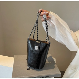 Detail of black glossy pleated leather bucket bag with silver chain strap and metal clasp