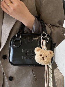 Minimalist black patent leather pillow bag with brown bear charm and woven lanyard