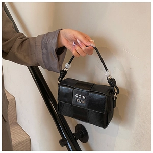 Close-up of black woven leather square handbag with metal logo and bead handle