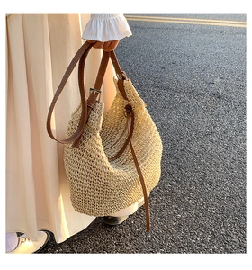 Close-up of casual straw tote bag featuring brown leather straps and gold metal buckles