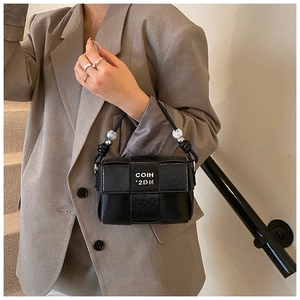 Detail of woven black leather mini bag featuring white letter print and beaded strap charms