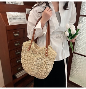 Straw tote bag detail with brown leather handles and decorative white cross stitching