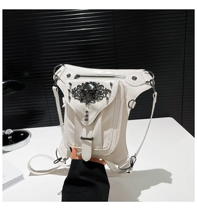 Detalle de riñonera gótica blanca con emblema de calavera negra y remaches plateados