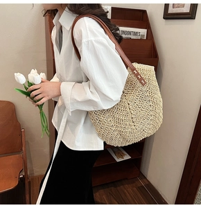 Detail of handwoven beige straw tote bag featuring brown leather straps and cross stitching