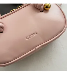 Detail of light pink leather bag featuring CLEAR OK embossed logo and gold sphere hardware