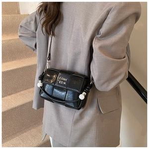 Close-up of black woven crossbody bag featuring silver metallic logo and white ball charm