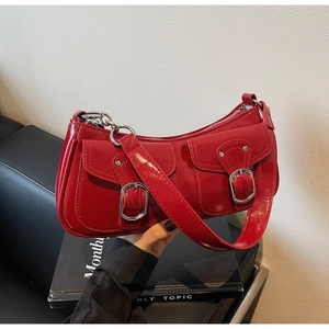 Detail view of red glossy patent leather shoulder bag with silver metal buckles