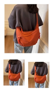 Detailed view of an orange crescent crossbody bag with woven rope zipper pulls on nylon