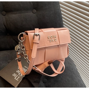 Détail d'un sac bandoulière tressé rose avec logo argenté, chaîne et pendentif