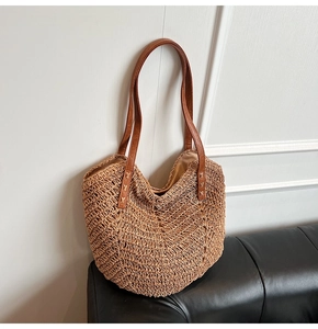Detail of woven straw tote bag with brown leather handles on a leather sofa