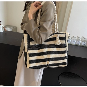 Detailed close-up of woven straw tote bag with contrast stripes and soft tassel accent