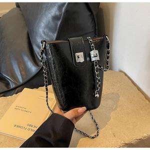 Detail of black glossy patent leather bucket bag with silver chain and metal clasp