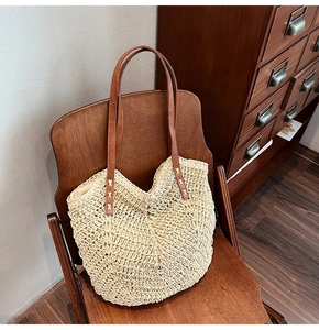 Detail of hand-woven straw tote with brown leather straps on a wooden chair