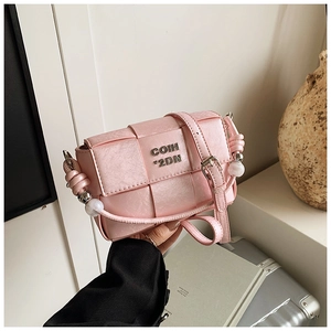 Close-up of pink woven handbag with metal lettering, pearl handle, and sleek PU leather texture