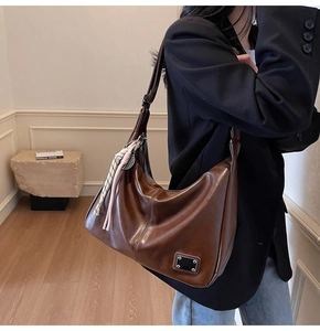 Detail of vintage brown leather crescent bag with metal buckle and woven scarf charm