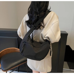 Adjustable woven strap and zipper detail of the black nylon half-moon crossbody bag