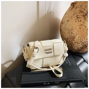 Detail view of woven cream white PU leather crossbody bag with metallic logo on art books
