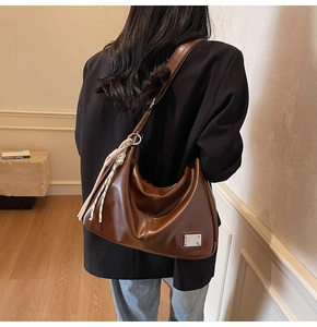 Brown leather hobo shoulder bag with silver plaque and decorative woven cord pendant