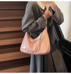 Pink hobo bag detail with metal logo plaque and decorative tassel charm on matte PU leather