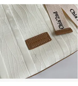 Close-up of wavy textured white tote fabric with leather logo tag and woven strap