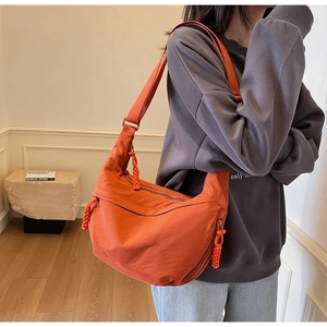 Detail view of orange nylon dumpling bag with hand-woven zipper pull and wide strap