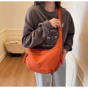 Detail of orange nylon dumpling crossbody bag with adjustable wide strap and cord zipper