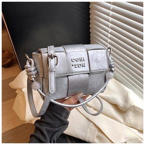 Close-up of silver woven handbag featuring metallic brand lettering and beaded handle detail