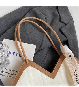 Detail of woven tote bag with brown leather trim and round handle on gray fabric