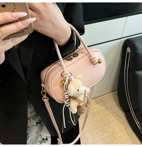Detail of pink PU leather Boston bag with plush bear charm and gold zipper accents