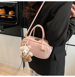 Modern light pink Boston bag with top handles and plush bear charm shown on a model