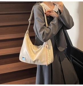 Close-up of cream leather tote bag with metal nameplate and colorful woven charm