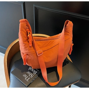 Detail of vibrant orange nylon half-moon bag with adjustable strap on a chair