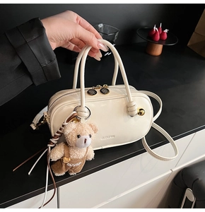 Detail view of cream Boston bag with plush bear charm and brand logo on leather surface