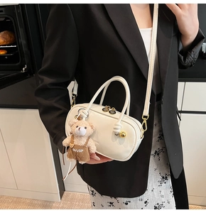 Detailed shot of white leather Boston bag with gold hardware and plush bear charm