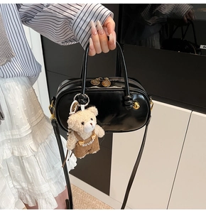 Detail of a black Boston bag featuring a teddy bear charm and sleek faux leather finish