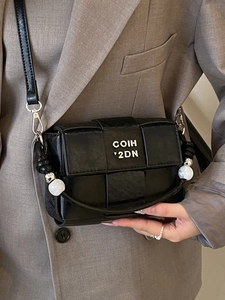 Chic black woven crossbody bag with marble bead details on a stylish brown suit