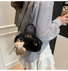 Detail of black patent leather Boston bag featuring golden zippers and a cute bear charm